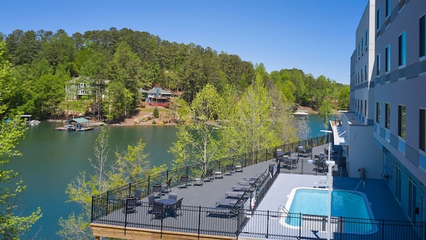 A poolside area with outdoor seating and a view of a lake and forested hills.