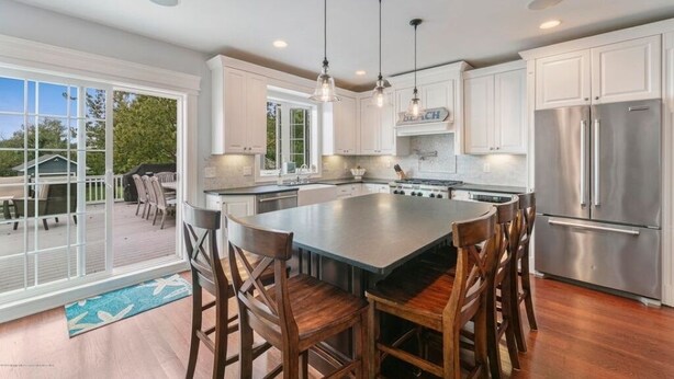 A modern kitchen with white cabinets, a large island with bar stools, stainless steel appliances, and pendant lighting.
