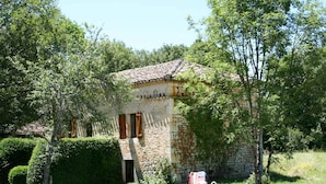 A stone building with a tiled roof, surrounded by lush greenery and a swimming pool.