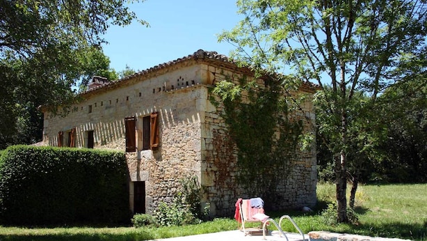 A stone building with a pool, surrounded by greenery.