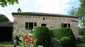 A stone building with a tiled roof, surrounded by well-maintained hedges and a grassy lawn.