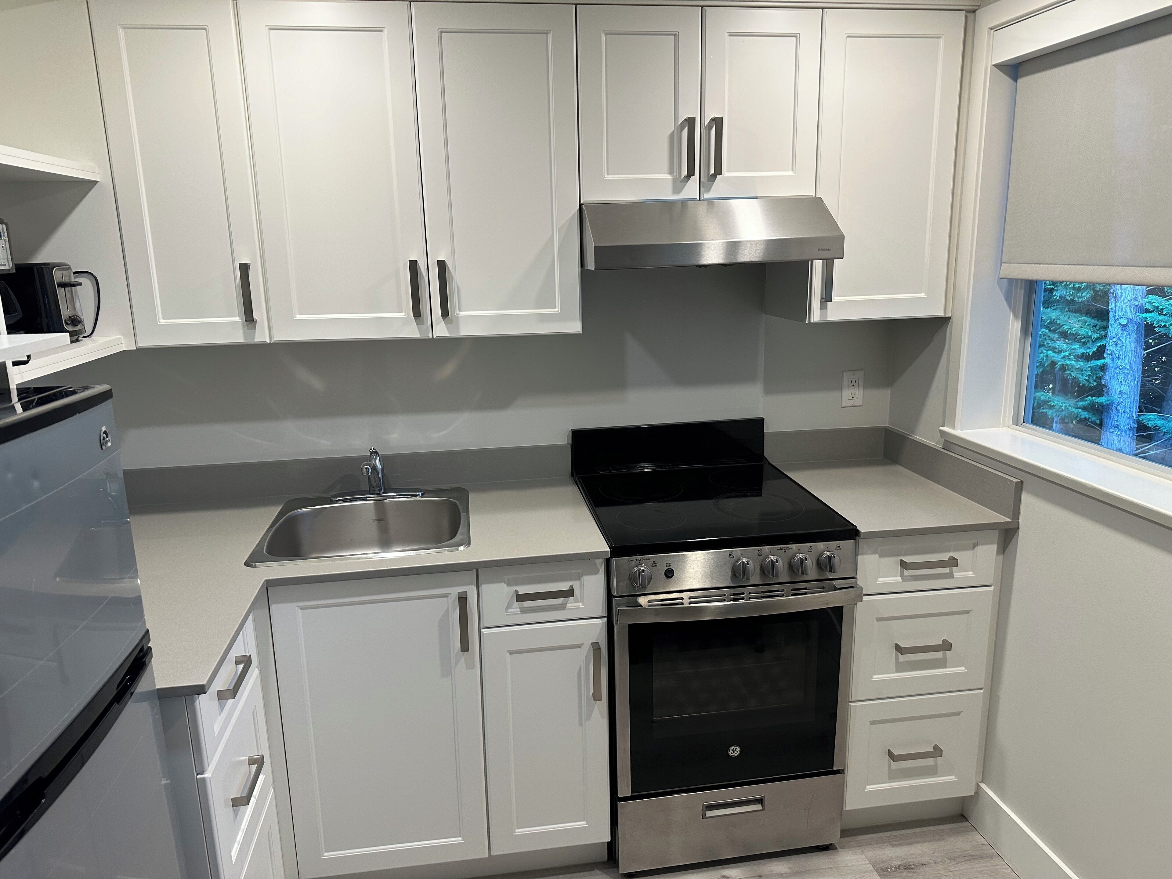 A modern kitchen with white cabinets, a stainless steel stove, and a window with a view of trees.