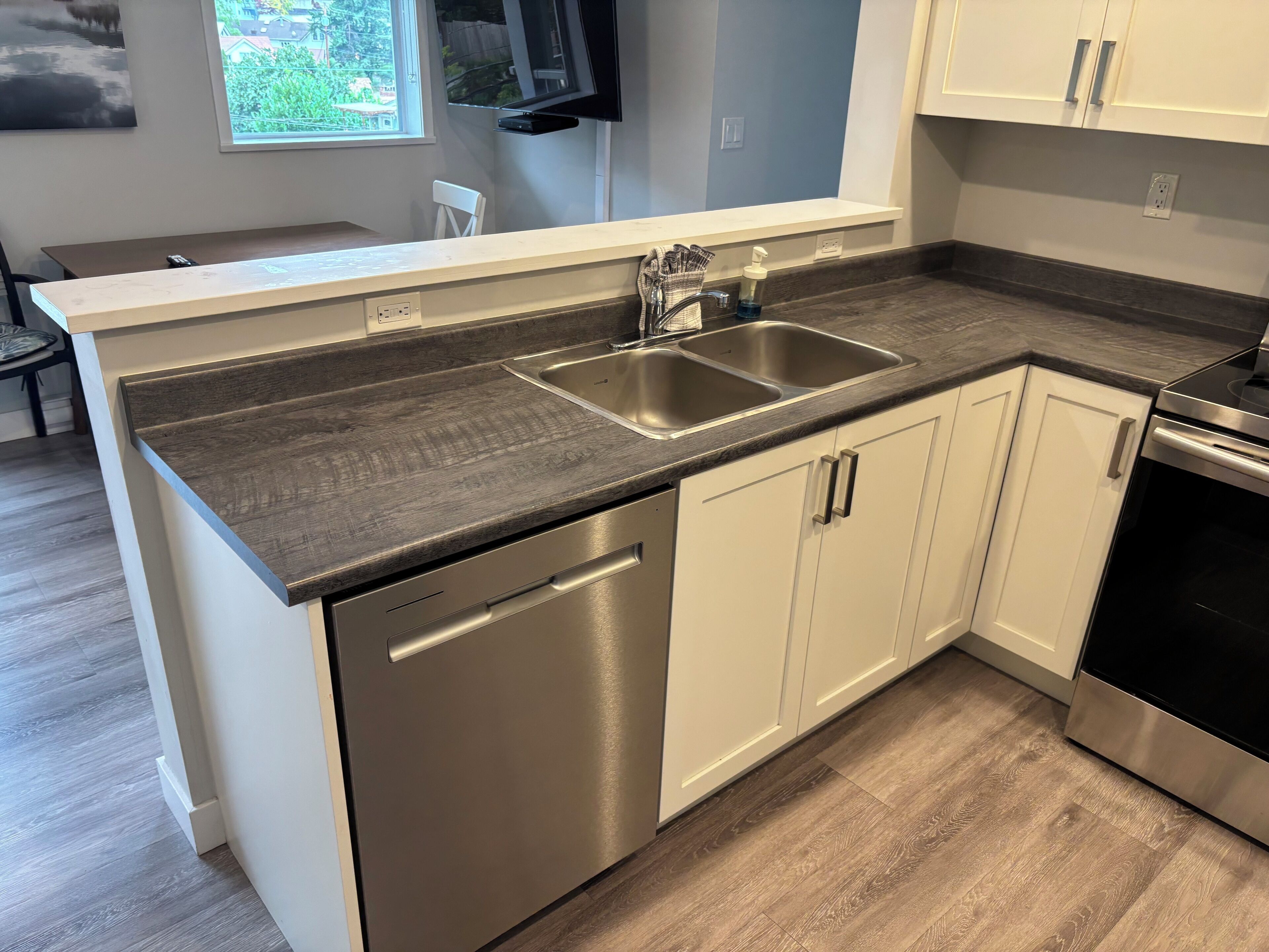 A modern kitchen with a stainless steel dishwasher, double sink, and white cabinets.