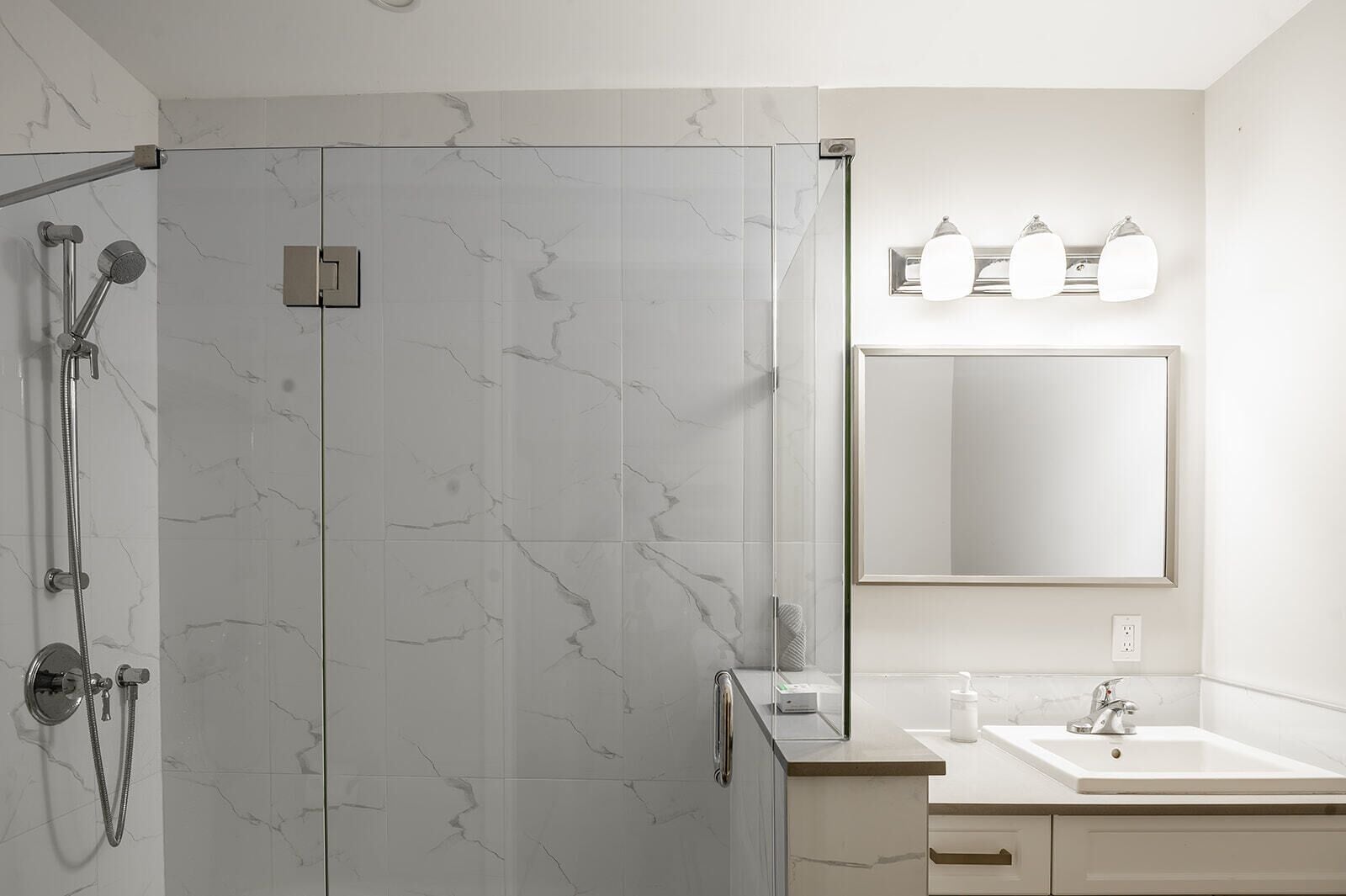 A modern bathroom with a glass-enclosed shower, a large mirror, and a white sink with a countertop.