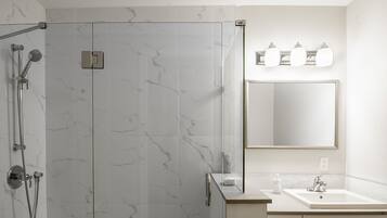 A modern bathroom with a glass-enclosed shower, a large mirror, and a white sink with a countertop.