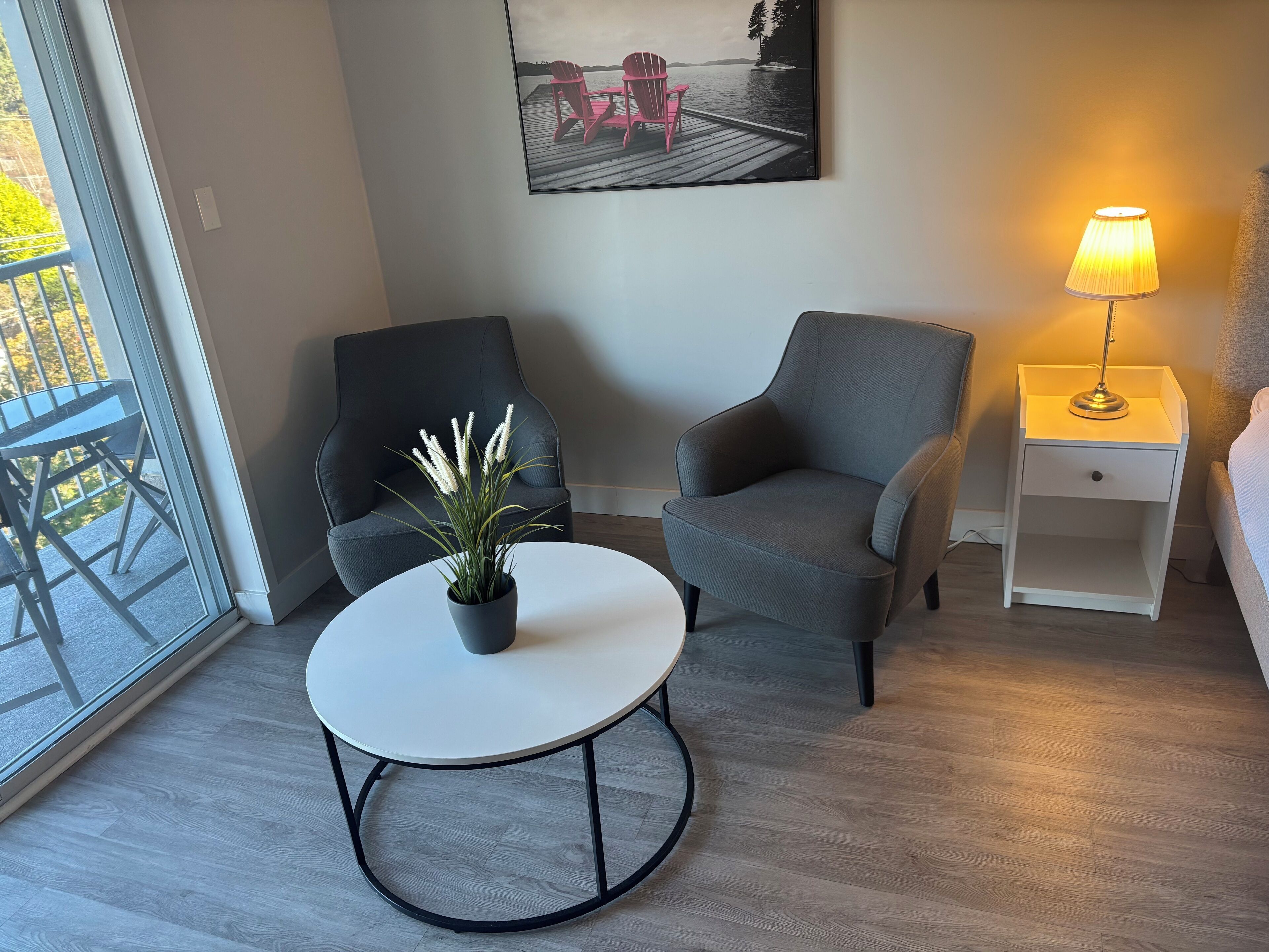 Een moderne woonkamer met een grijze bank, een witte salontafel, een potplant, een lamp en een schilderij van een steiger.