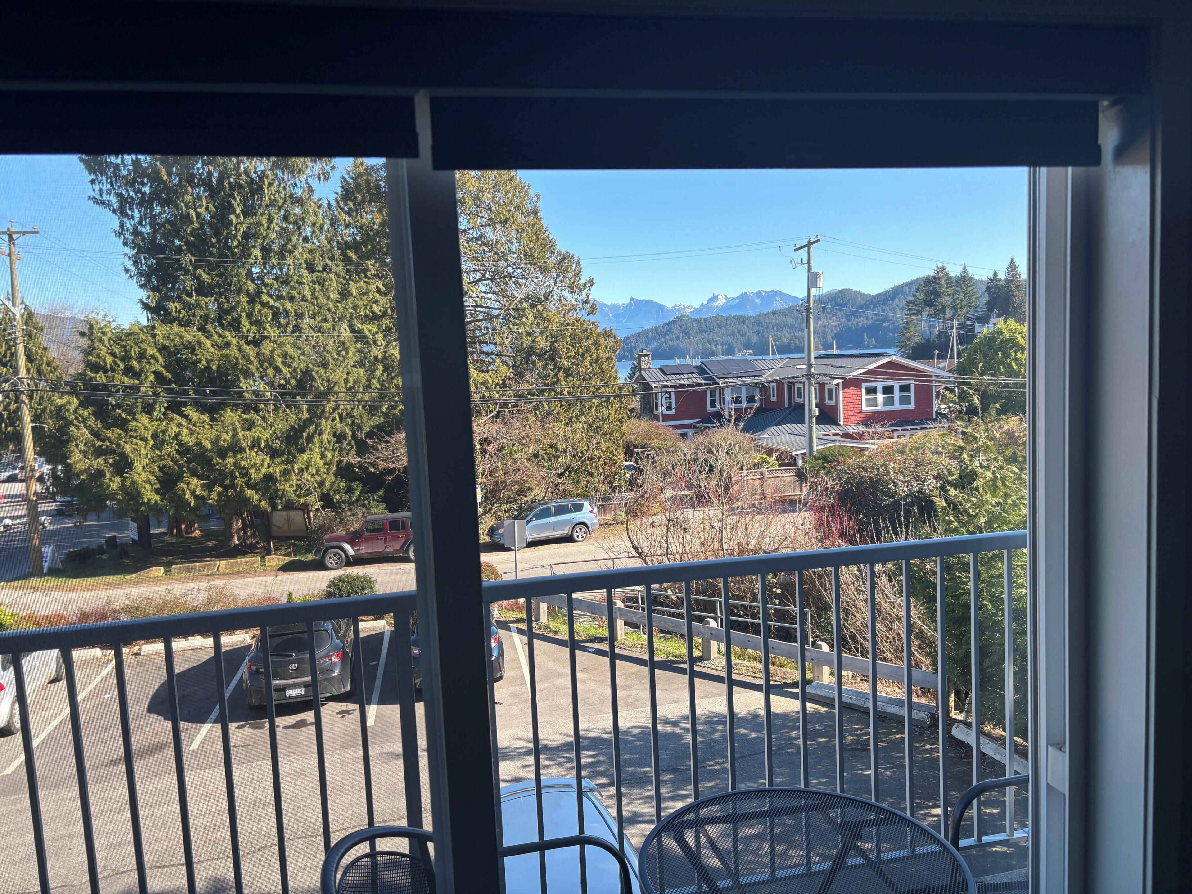Un balcon donnant sur un parking, des arbres et une maison rouge.