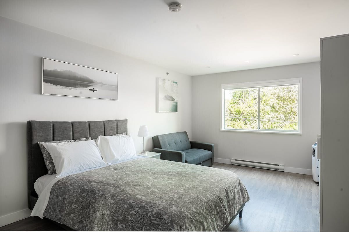 A bedroom with a bed, a chair, a window with a view of trees, and a heater on the floor.