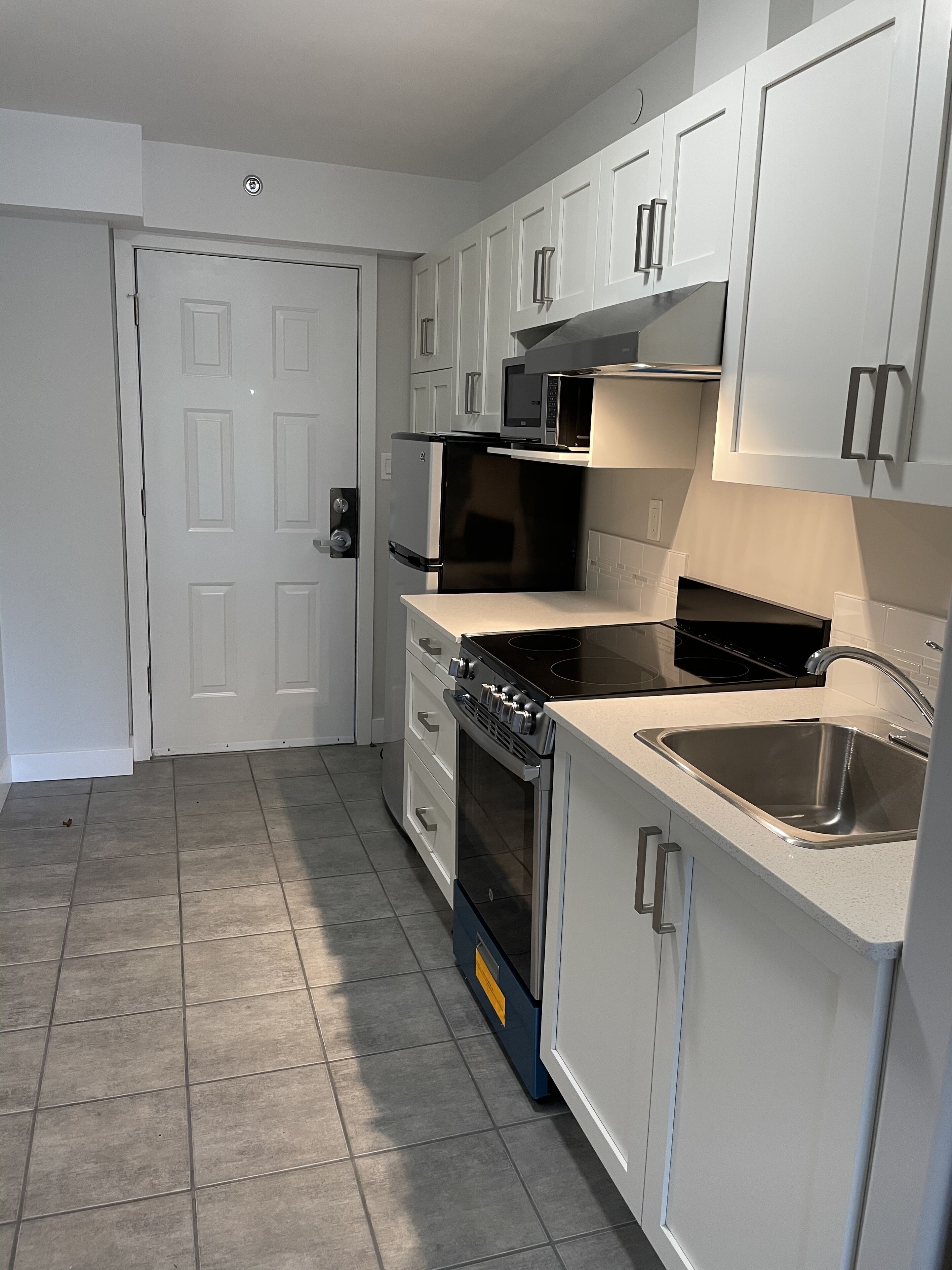 A compact kitchen with white cabinets, a built-in microwave, a stove, and a sink.