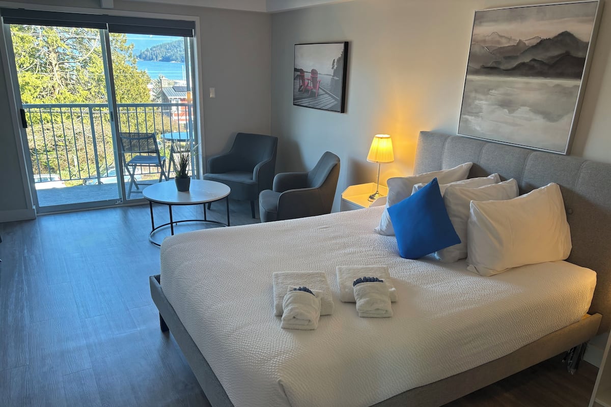 A hotel room with a bed, a desk, a chair, a table, and a balcony with a view.