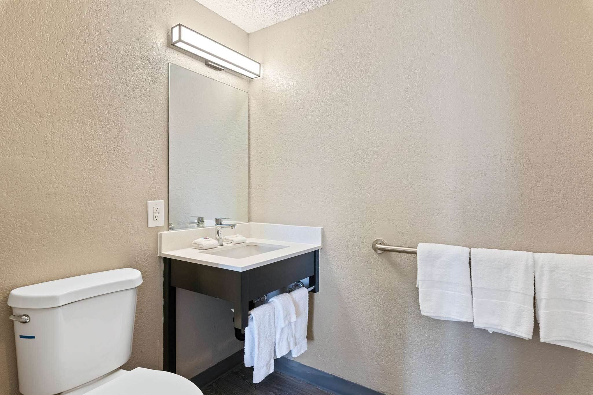 A bathroom with a white toilet, a sink, and a towel rack with three towels.