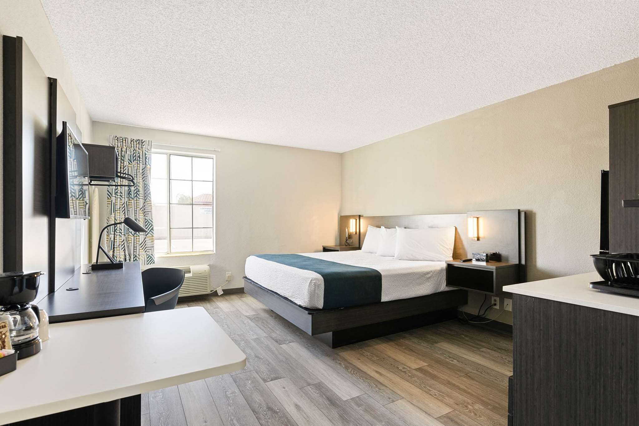 A modern hotel room with a bed, bedside table, lamp, and a view of the outside through a window.