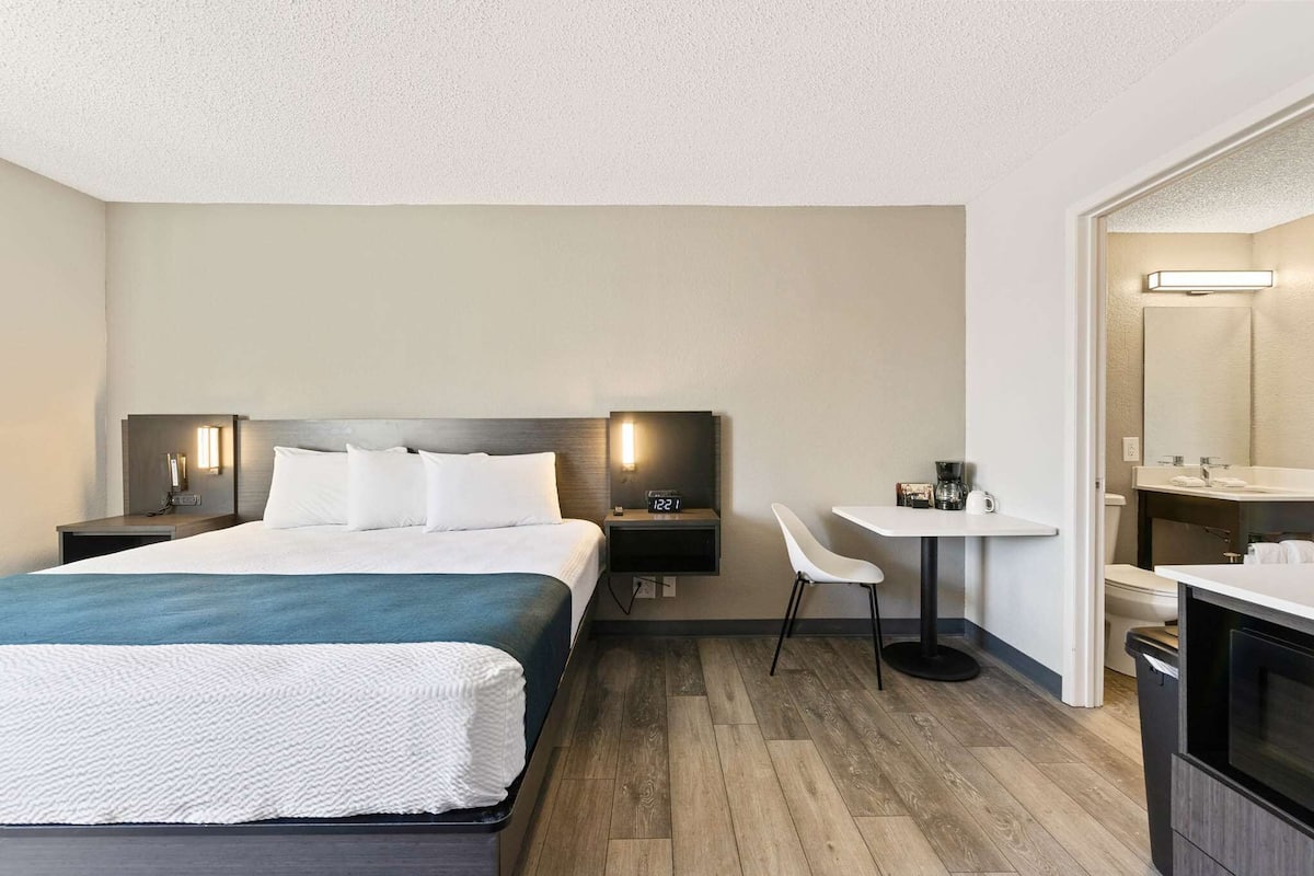 Une chambre d’hôtel avec un grand lit, des tables de chevet, un bureau avec une chaise, un miroir et une petite kitchenette.