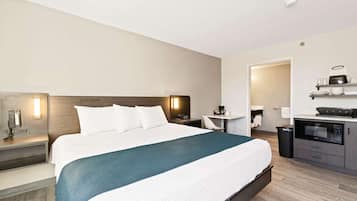 Habitación de hotel con una cama grande, mesitas de noche, un escritorio, un microondas y un cubo de basura pequeño.
