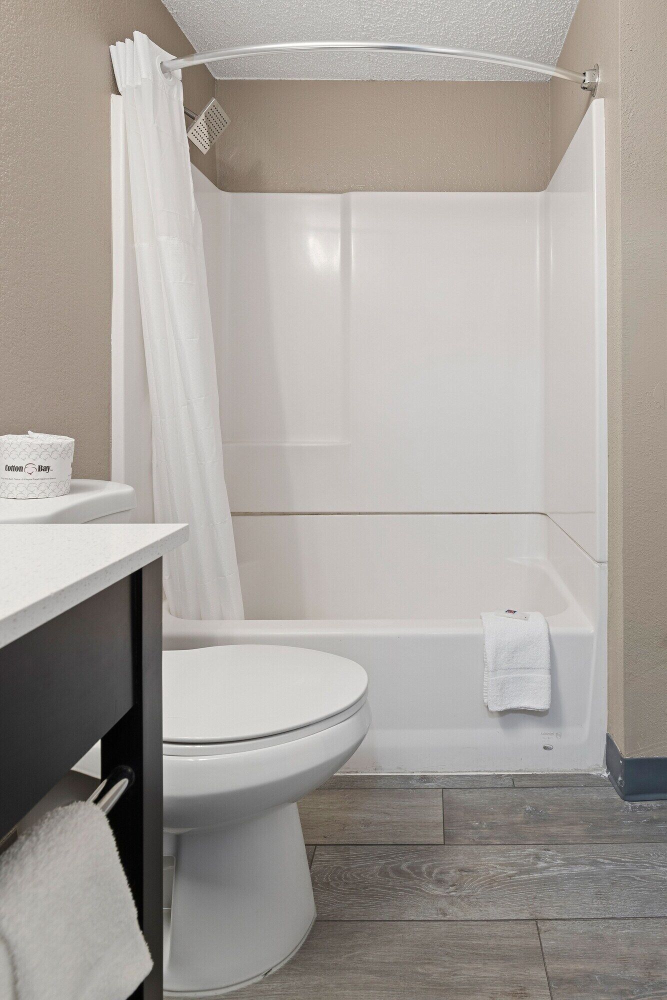 A bathroom with a toilet, a shower with a white curtain, a bathtub, and a towel on the floor.