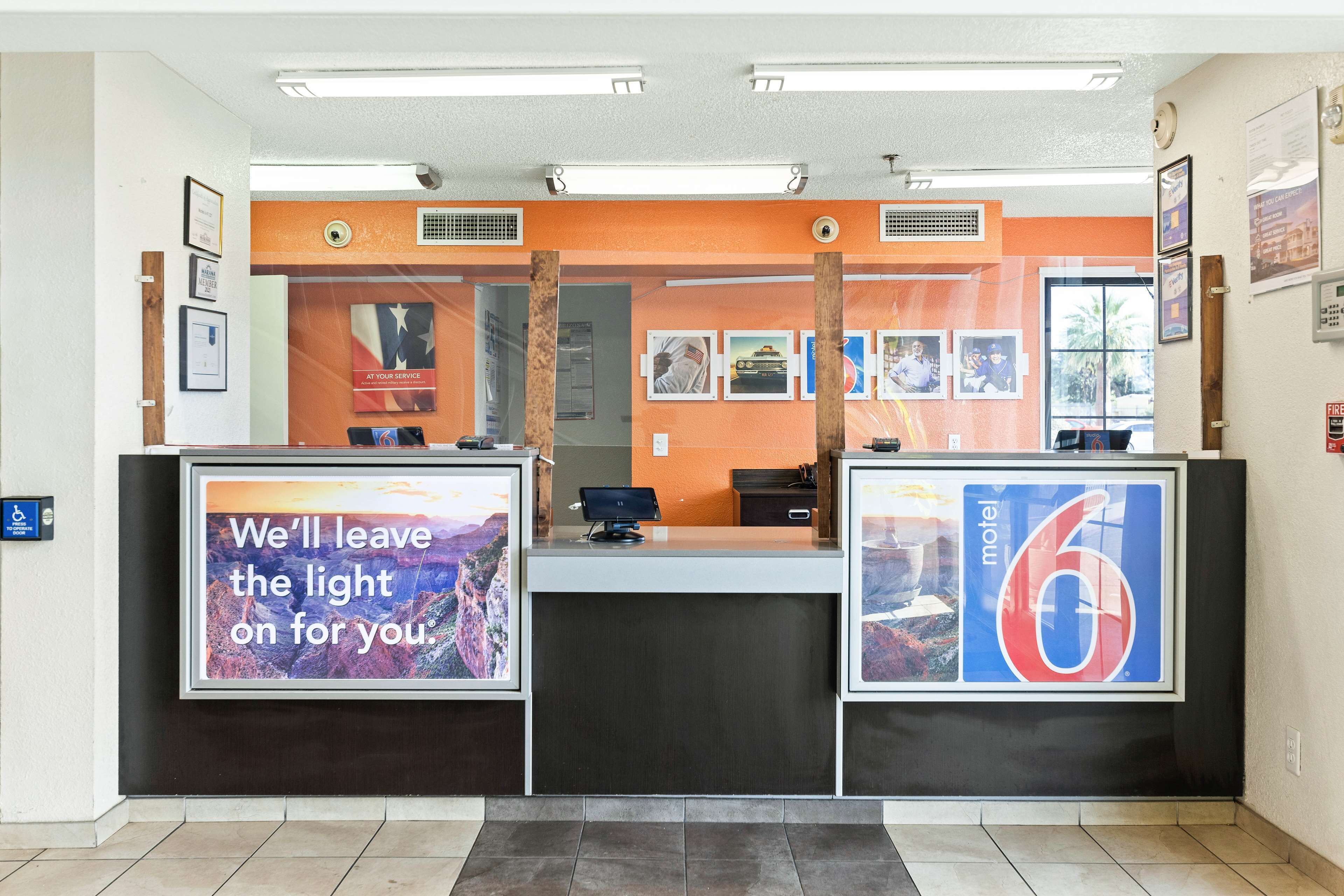 A hotel reception area with a counter, framed pictures on the wall, and a sign for 'motel 6'.
