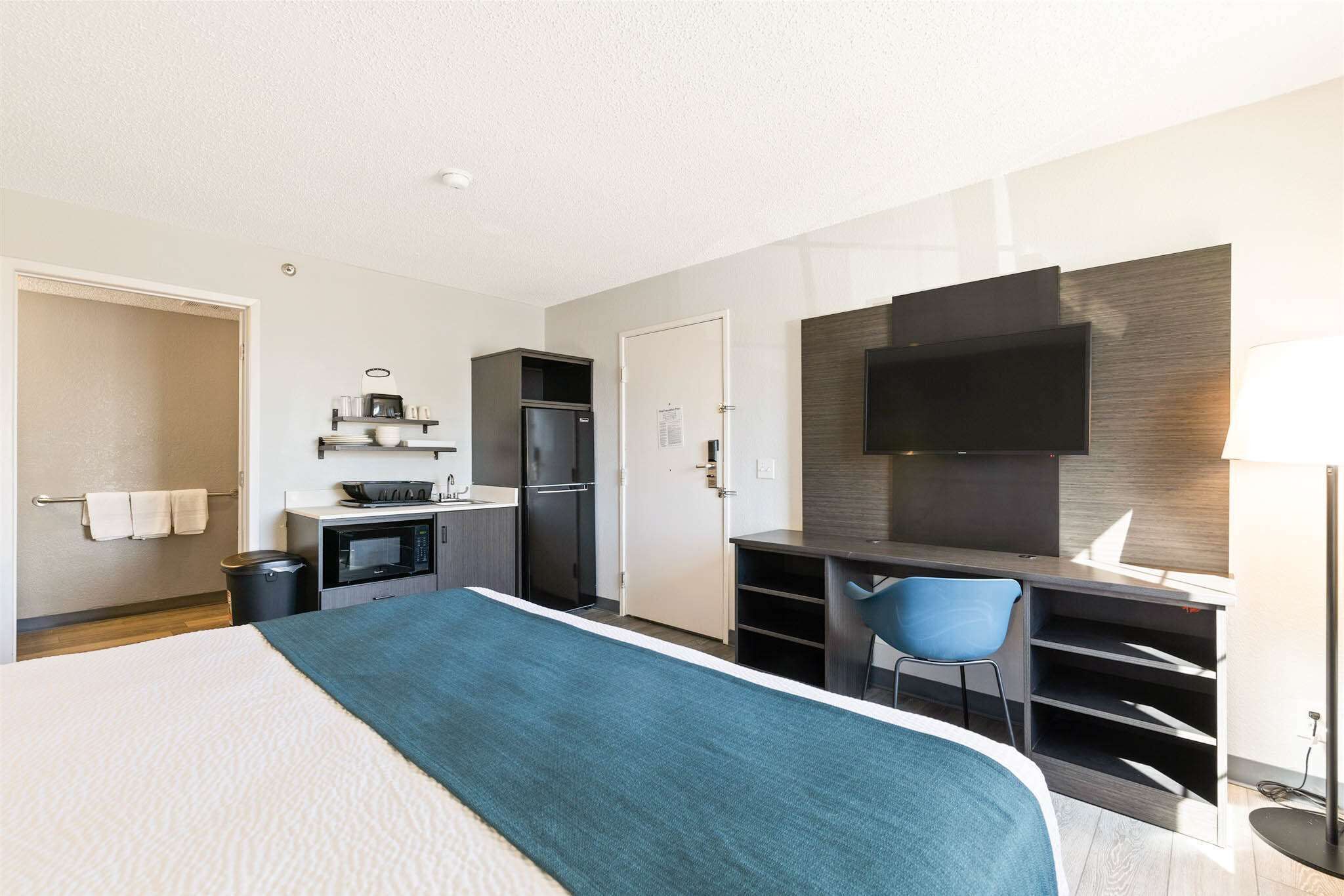 A hotel room with a bed, a desk, a chair, a TV, a microwave, and a small kitchenette.