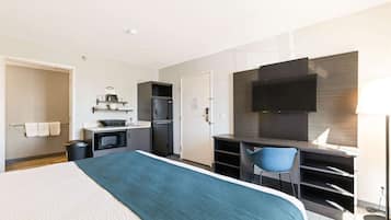 A hotel room with a bed, a desk, a chair, a TV, a microwave, and a small kitchenette.