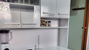 Keittiössä on valkoiset kaapit, tehosekoitin ja pesuallas.