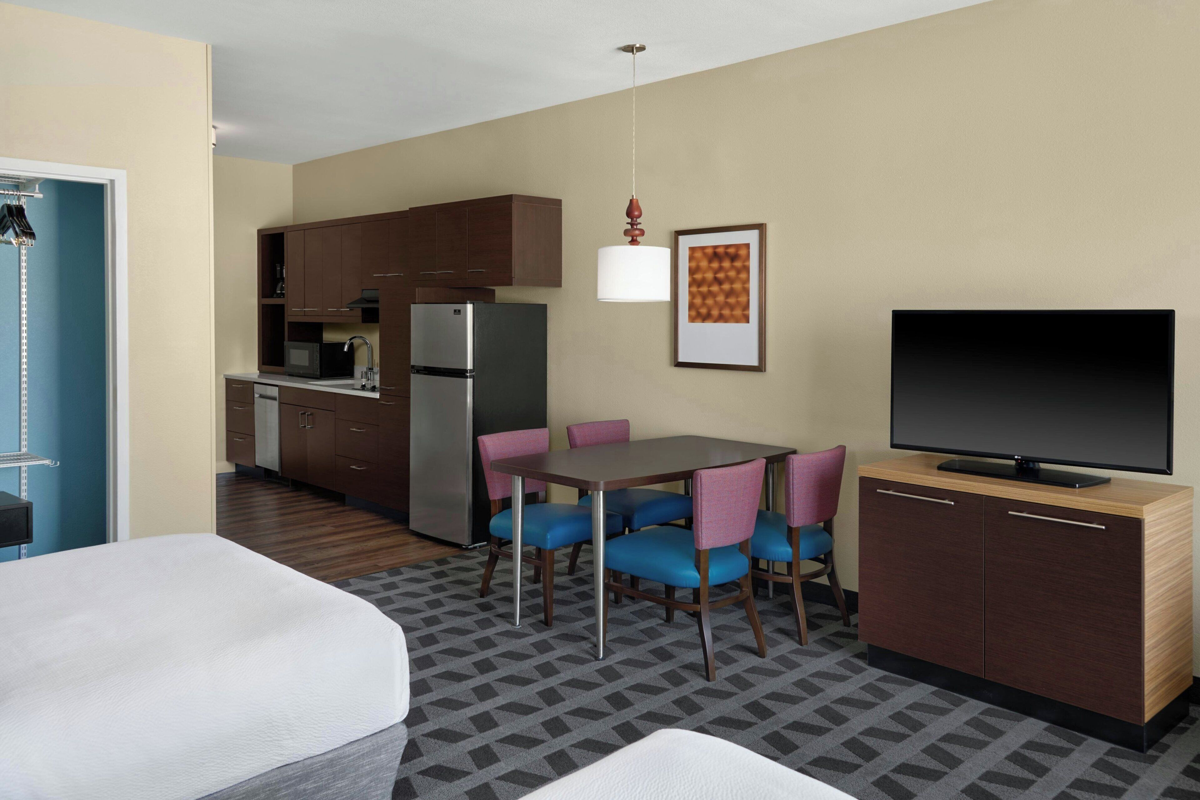 A compact hotel room with a kitchenette, a dining area with chairs, a television, and a bed.