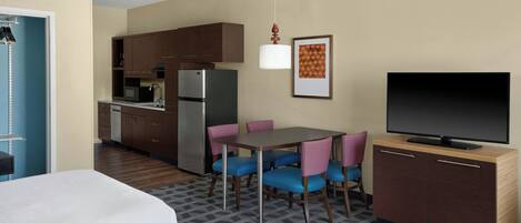 A compact hotel room with a kitchenette, a dining area with chairs, a television, and a bed.
