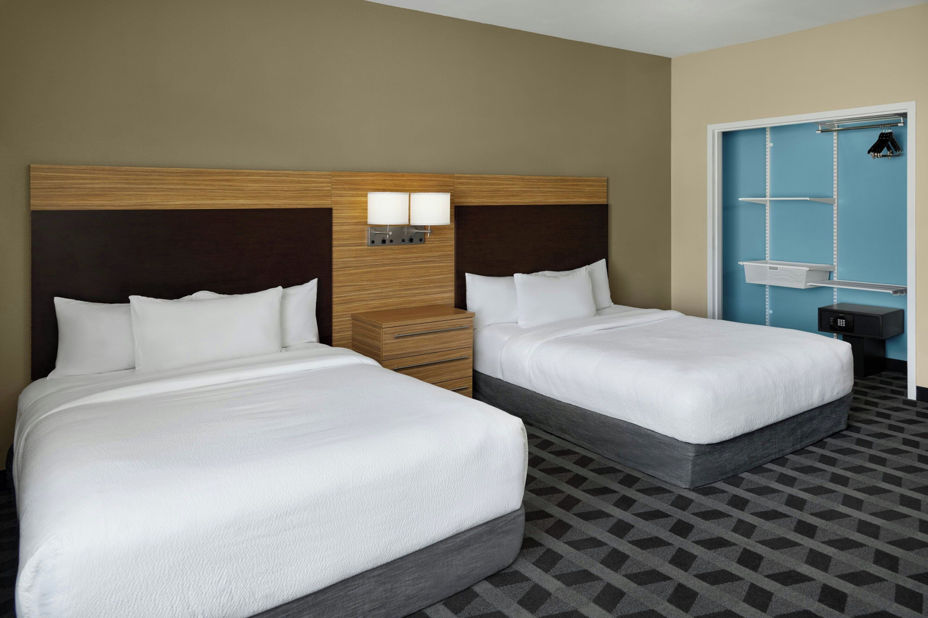 A hotel room with two beds, a nightstand, a wall-mounted lamp, and a wardrobe with hanging space.