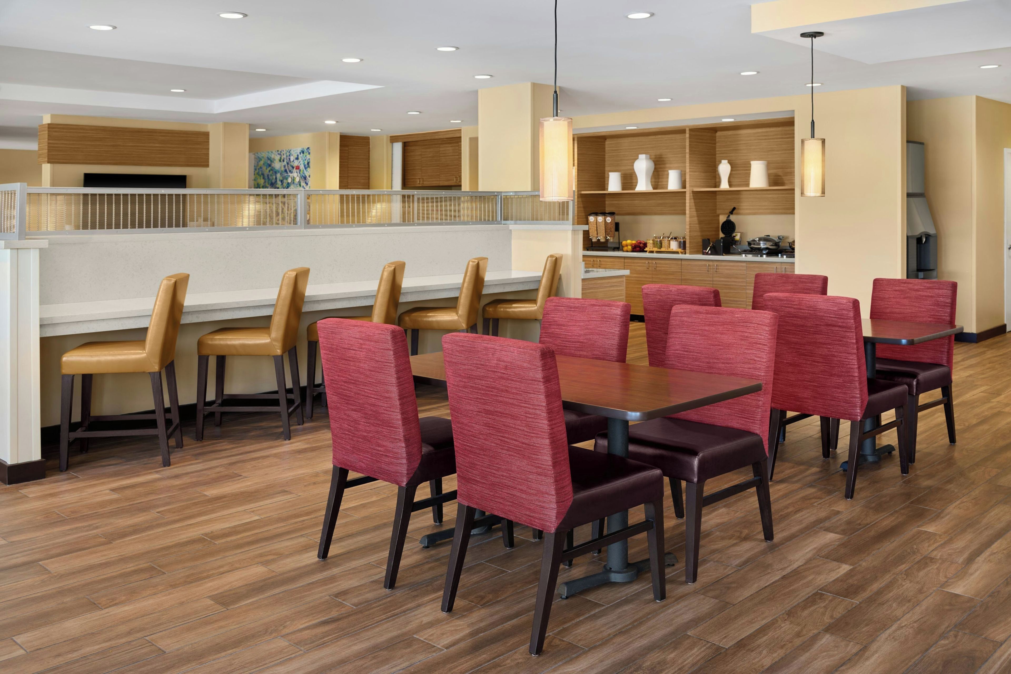 A restaurant with multiple tables and chairs, a kitchen area, and a counter.