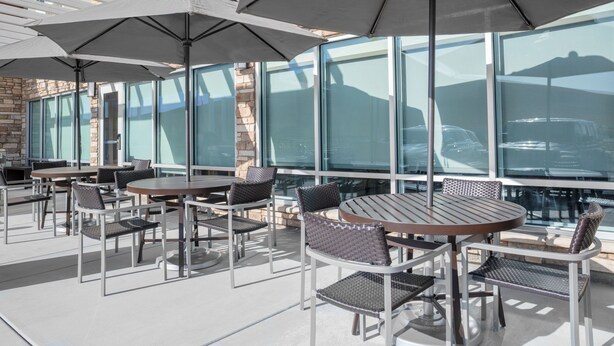 Une terrasse extérieure avec des tables et des chaises rondes, de grands parasols et une vue sur une montagne, visible à travers de grandes fenêtres.