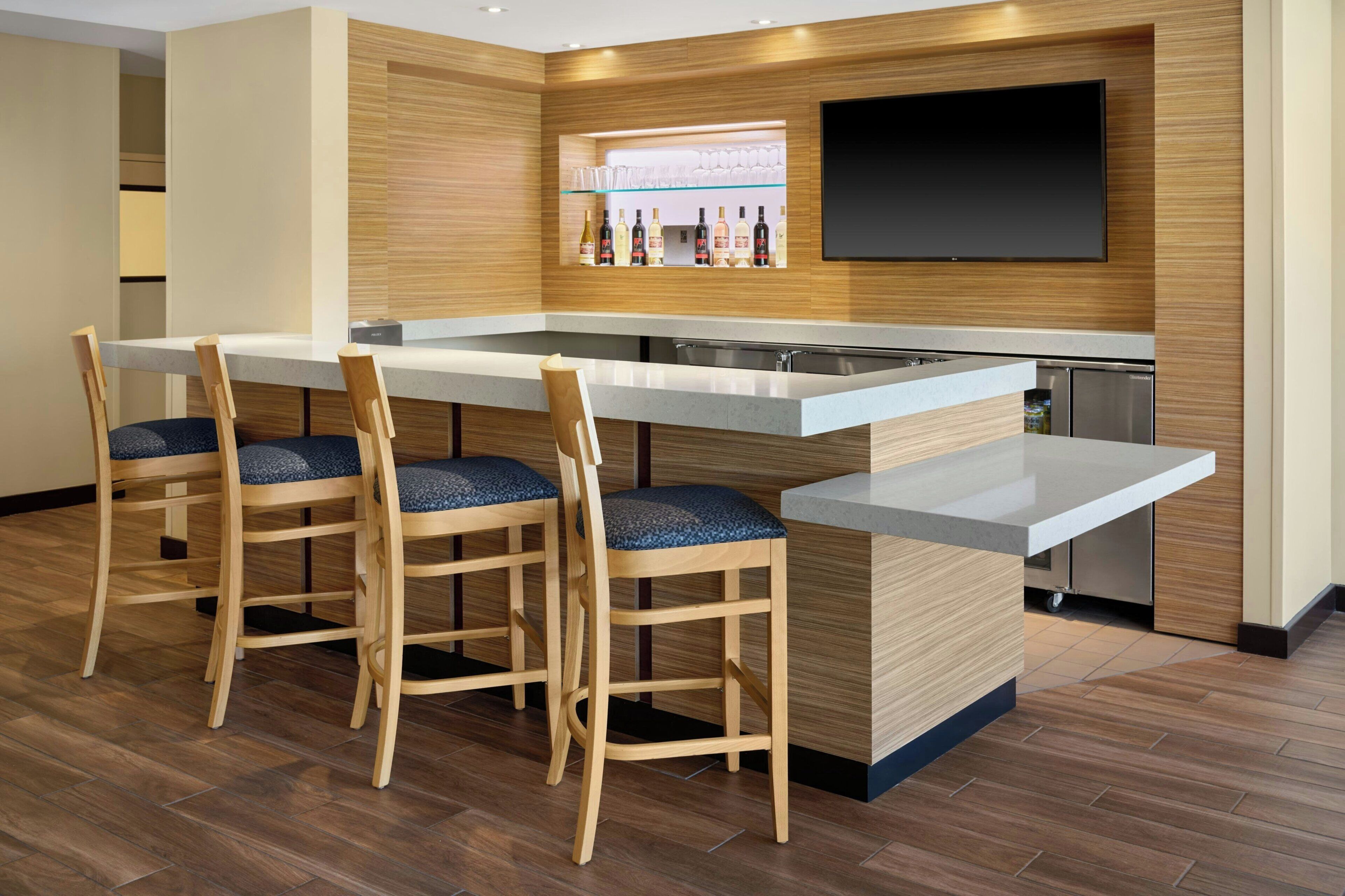A modern kitchen with a bar area, wooden chairs, and a flat-screen TV.