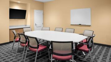A conference room with a white table, red and black chairs, a whiteboard, a flat-screen TV, and a door.