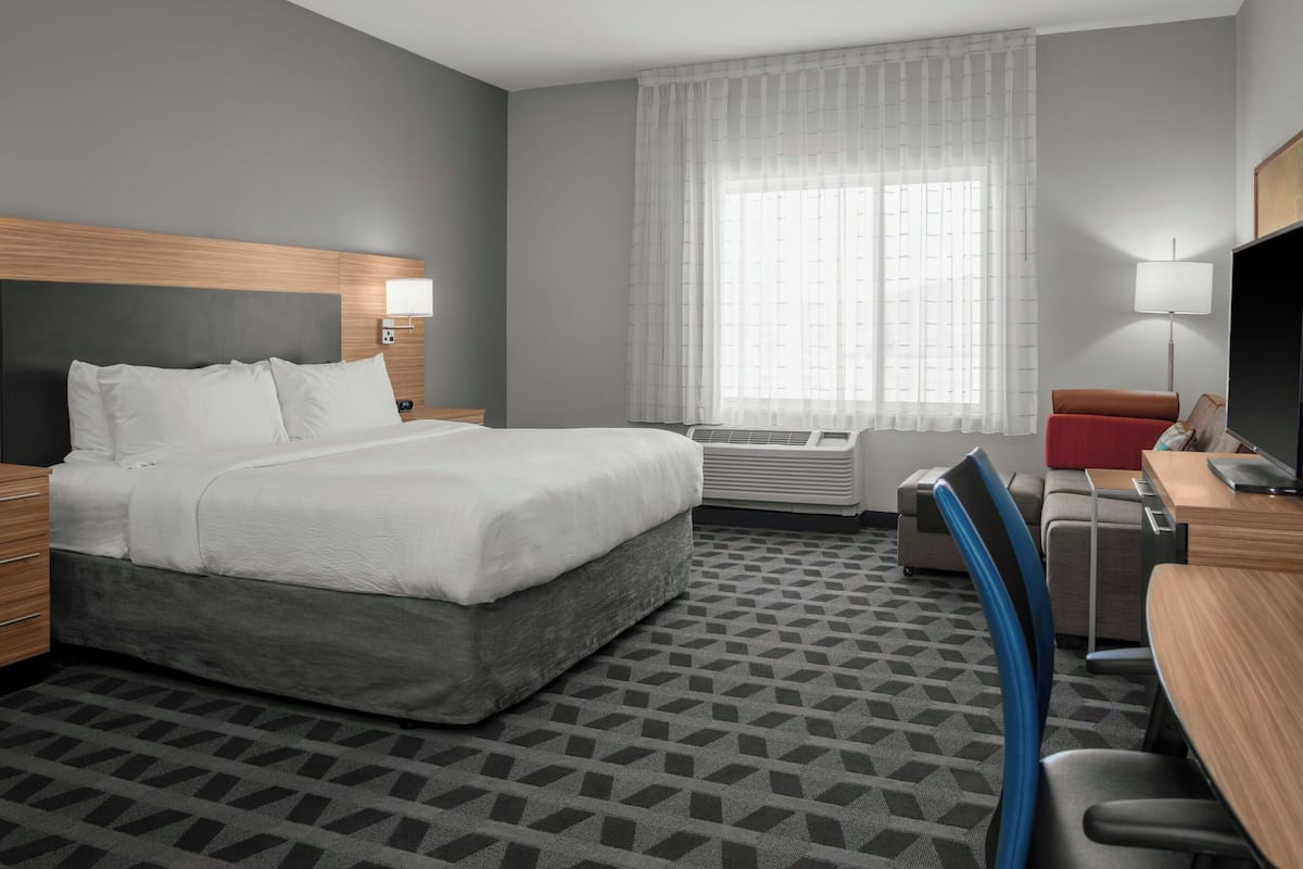 Una habitación de hotel con cama, escritorio, silla y un ventanal con cortinas.