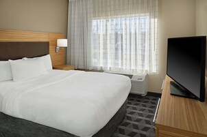 Habitación de hotel con una cama grande, televisión, lámpara de noche y ventana con cortinas.
