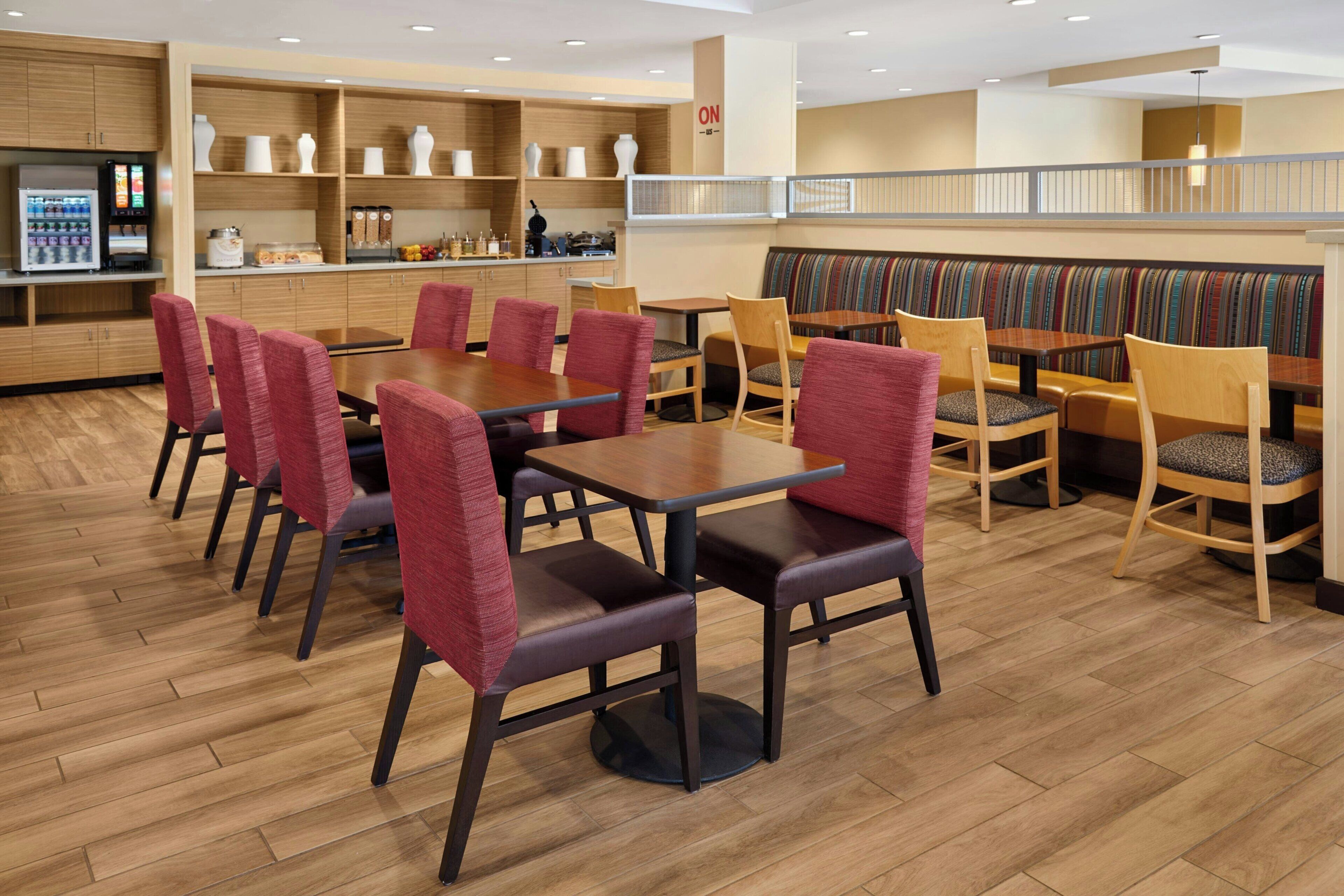 Un espace de restauration moderne avec un plancher en bois, des chaises à revêtement rouge et divers types de sièges, notamment des banquettes et des tables.