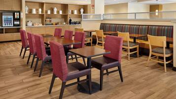 Un espace de restauration moderne avec un plancher en bois, des chaises à revêtement rouge et divers types de sièges, notamment des banquettes et des tables.