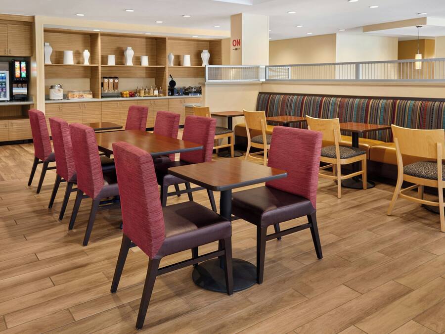Un espace de restauration moderne avec un plancher en bois, des chaises à revêtement rouge et divers types de sièges, notamment des banquettes et des tables.