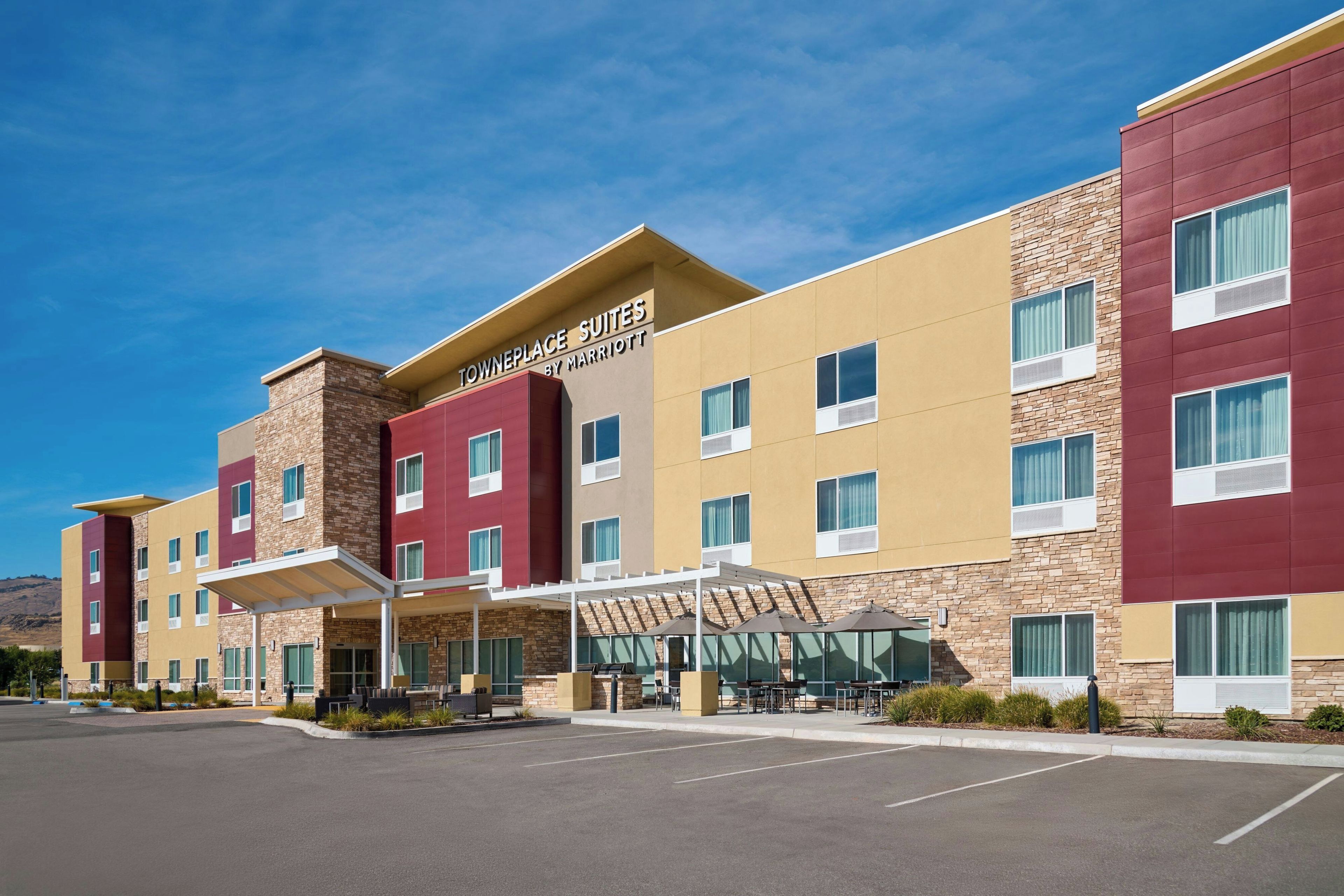 A hotel with a modern design, featuring a mix of red and beige colors, and a clear sky.