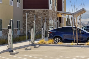 Un estacionamiento con estaciones de carga para vehículos eléctricos, un coche azul y un edificio de fachada de piedra y madera.