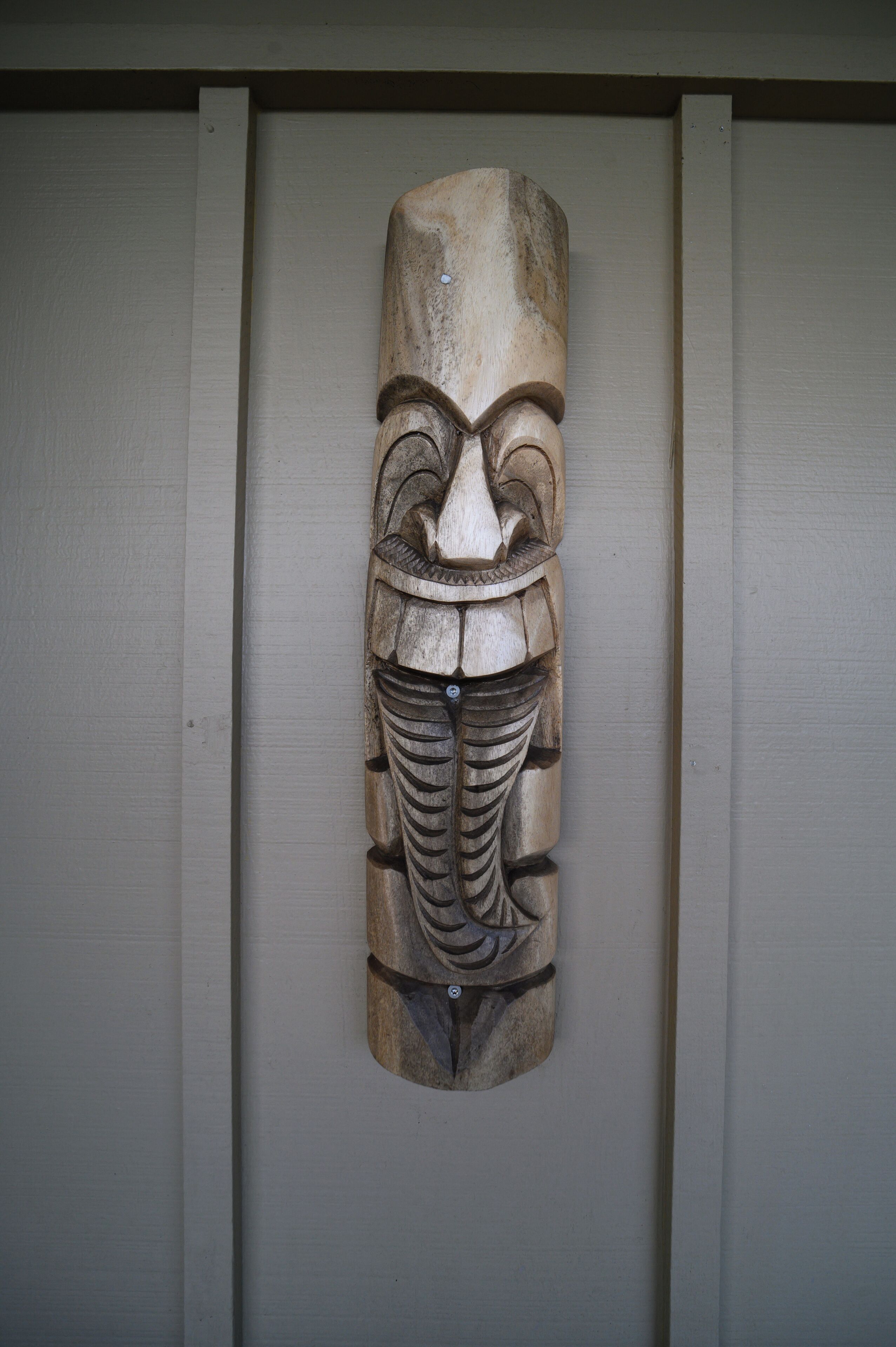 En utskuren trästaty, formad som en totem, som är upphängd på en vägg.