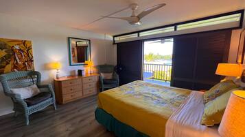 A hotel room with a bed, a desk, a chair, a ceiling fan, and a view of the outdoors.