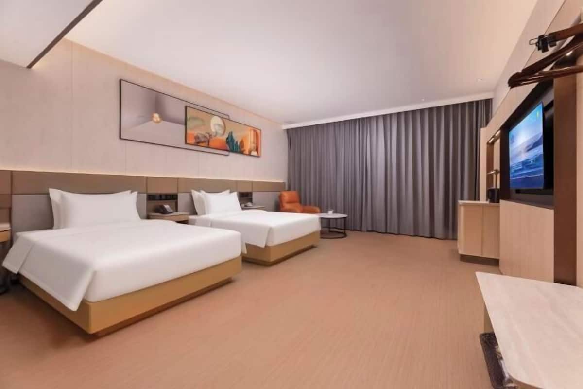 A hotel room with two beds, a TV, a desk, and a chair.