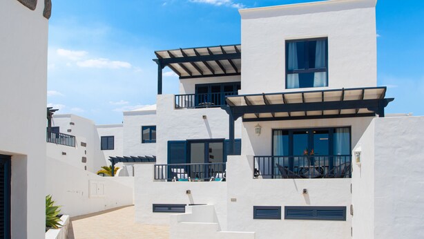 A modern building with white walls and blue accents, featuring balconies and outdoor seating areas. - Villa Arosa - Spectacular duplex in Playa Blanca (Playa Blanca)