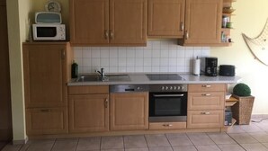 Een keuken met houten kastjes, een magnetron, een vaatwasser, een fornuis en een spoelbak.