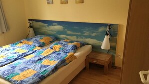Een bed met een kleurrijke quilt, een nachtkastje en een wandlamp.