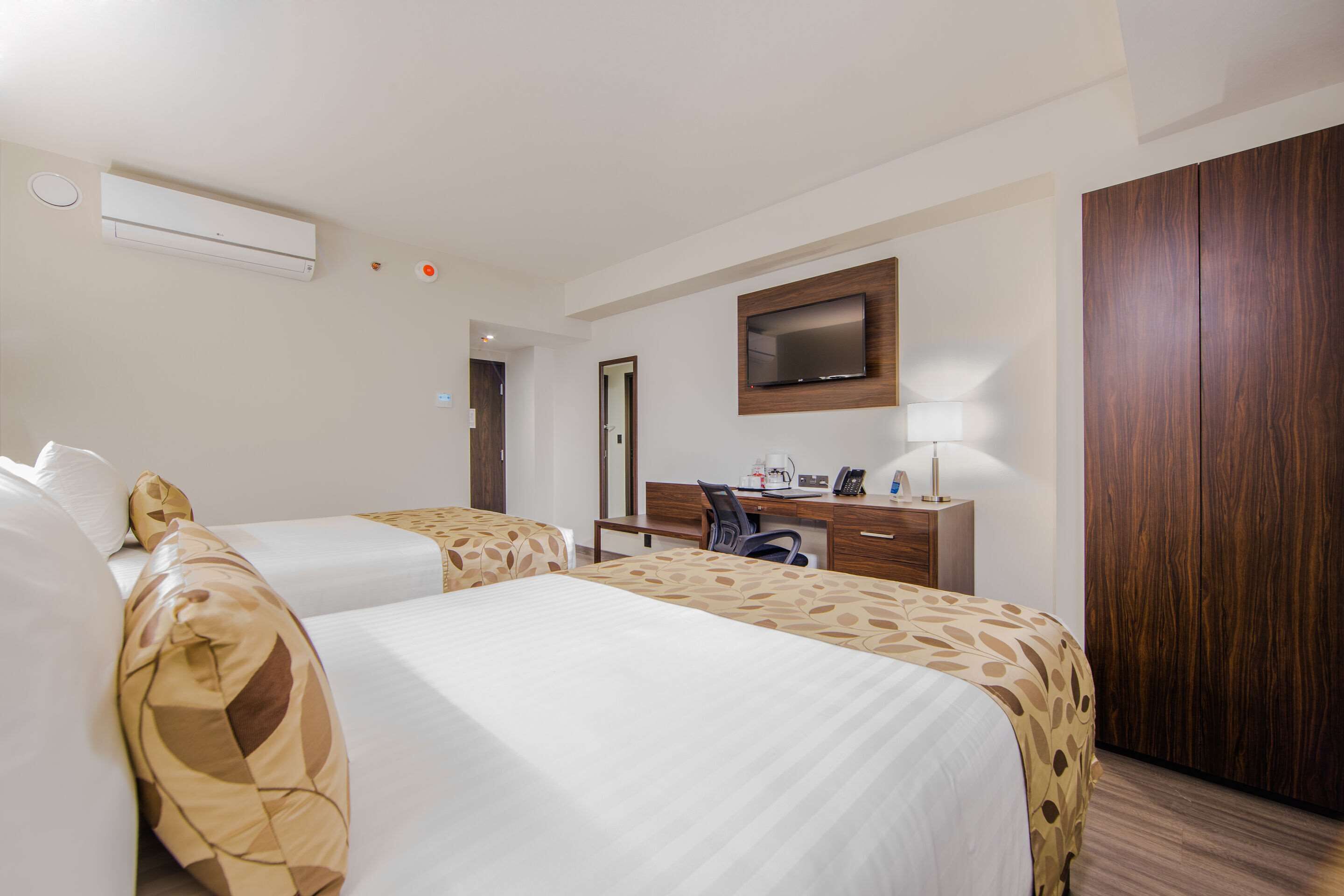 Hotelkamer met twee bedden, een bureau met stoel, een wandtelevisie en een kledingkast.