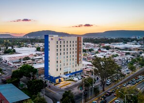 Um hotel alto com vários andares, uma placa chamativa com a palavra 'Sleep' e vista da área urbana circundante, com ruas e outros edifícios.