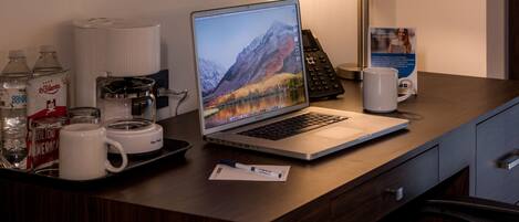 Un bureau d’hôtel avec un ordinateur portable, une machine à café, un téléphone et divers objets disposés sur un plateau.