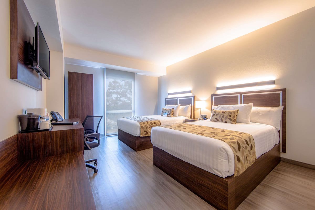 Una habitación de hotel con dos camas, un escritorio, un televisor de pantalla plana y un ventanal grande.
