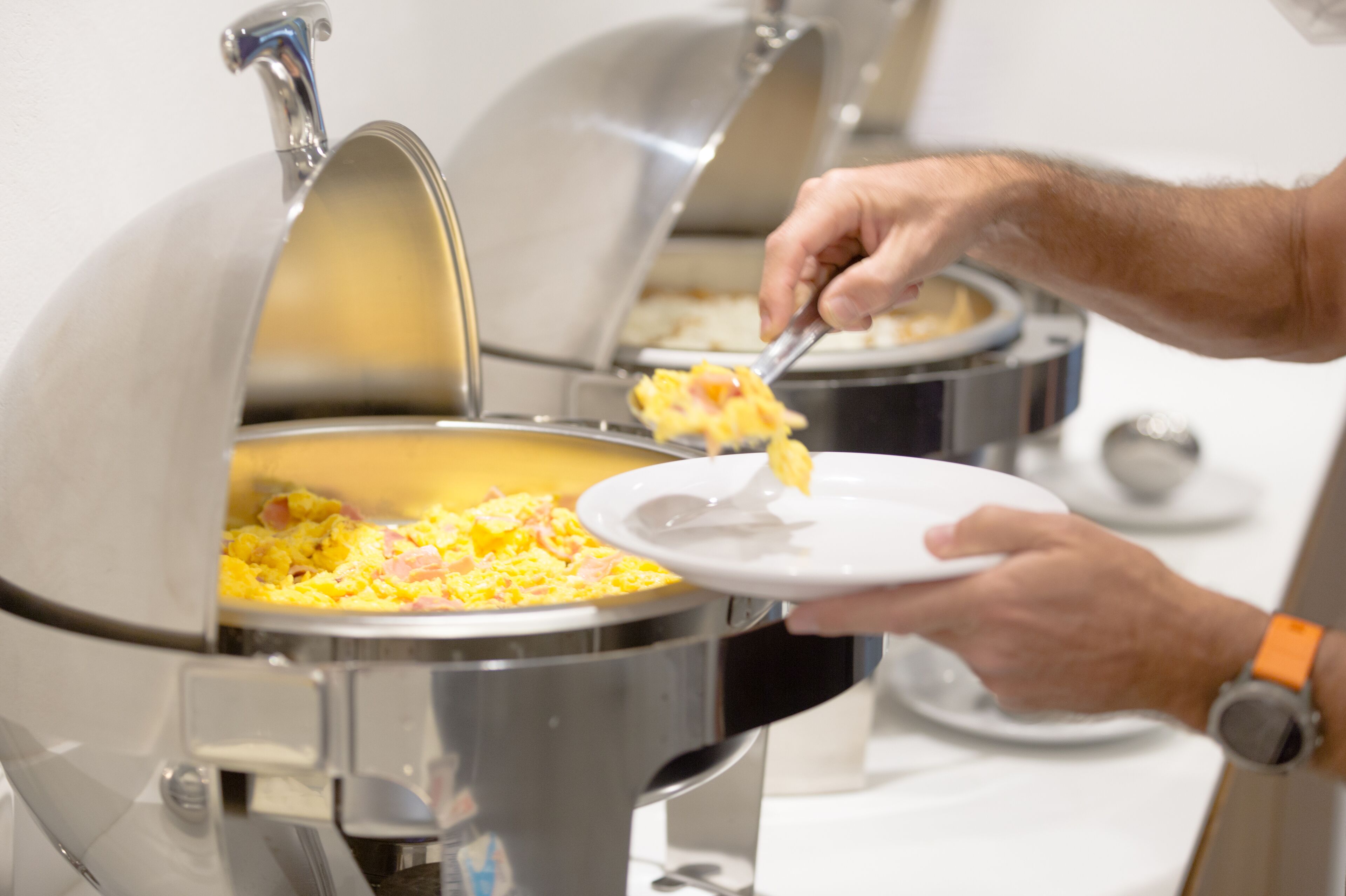 A buffet setup with a person serving scrambled eggs.