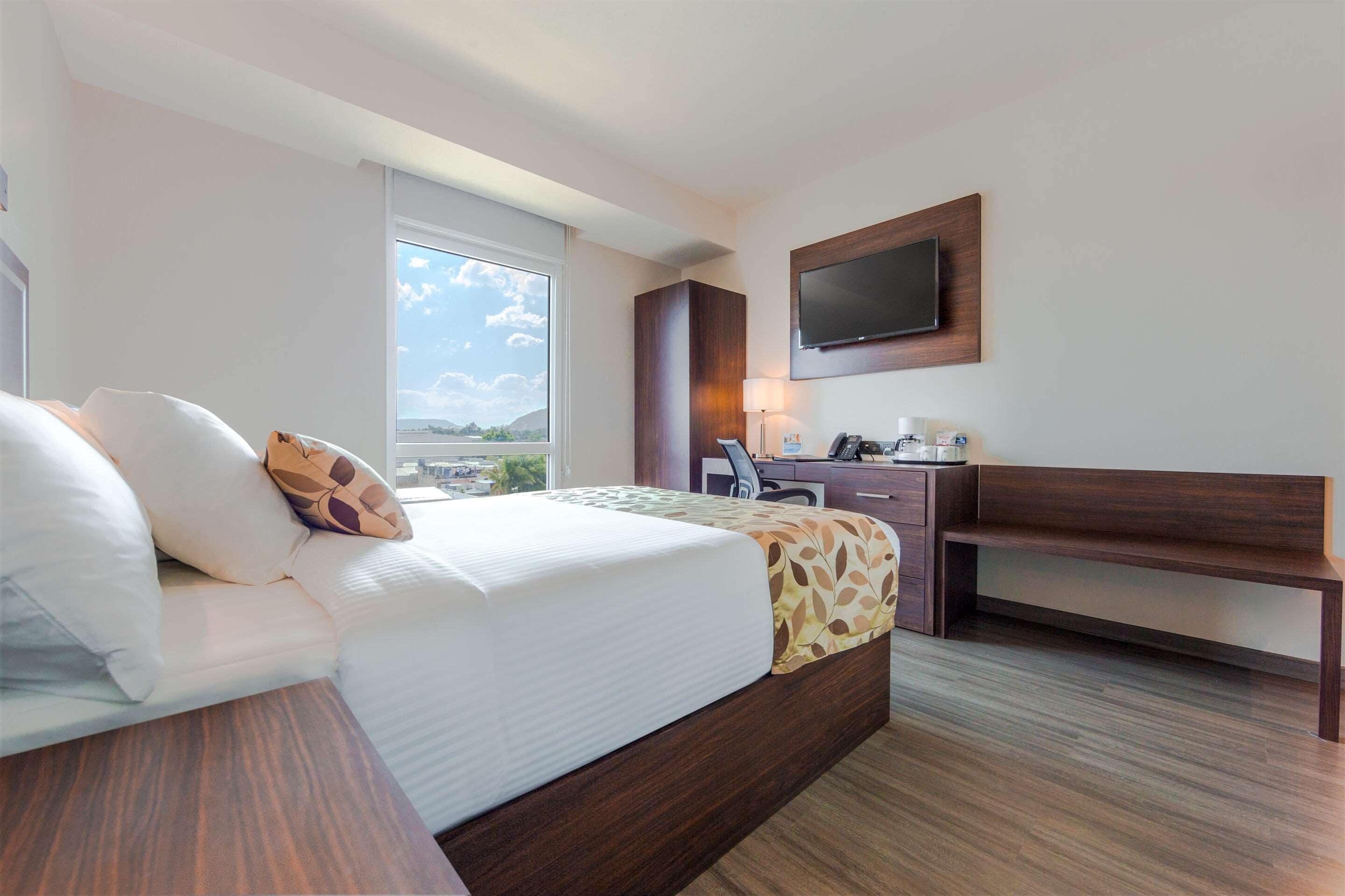 Une chambre d’hôtel équipée d’un lit, d’un bureau, d’une chaise, d’une télévision et d’une fenêtre donnant sur un paysage agréable.