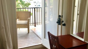 Ein Zimmer mit Holzboden, einem kleinen Tisch mit Stuhl, einer Tür zu einem Balkon und einer Fußmatte im Eingangsbereich.